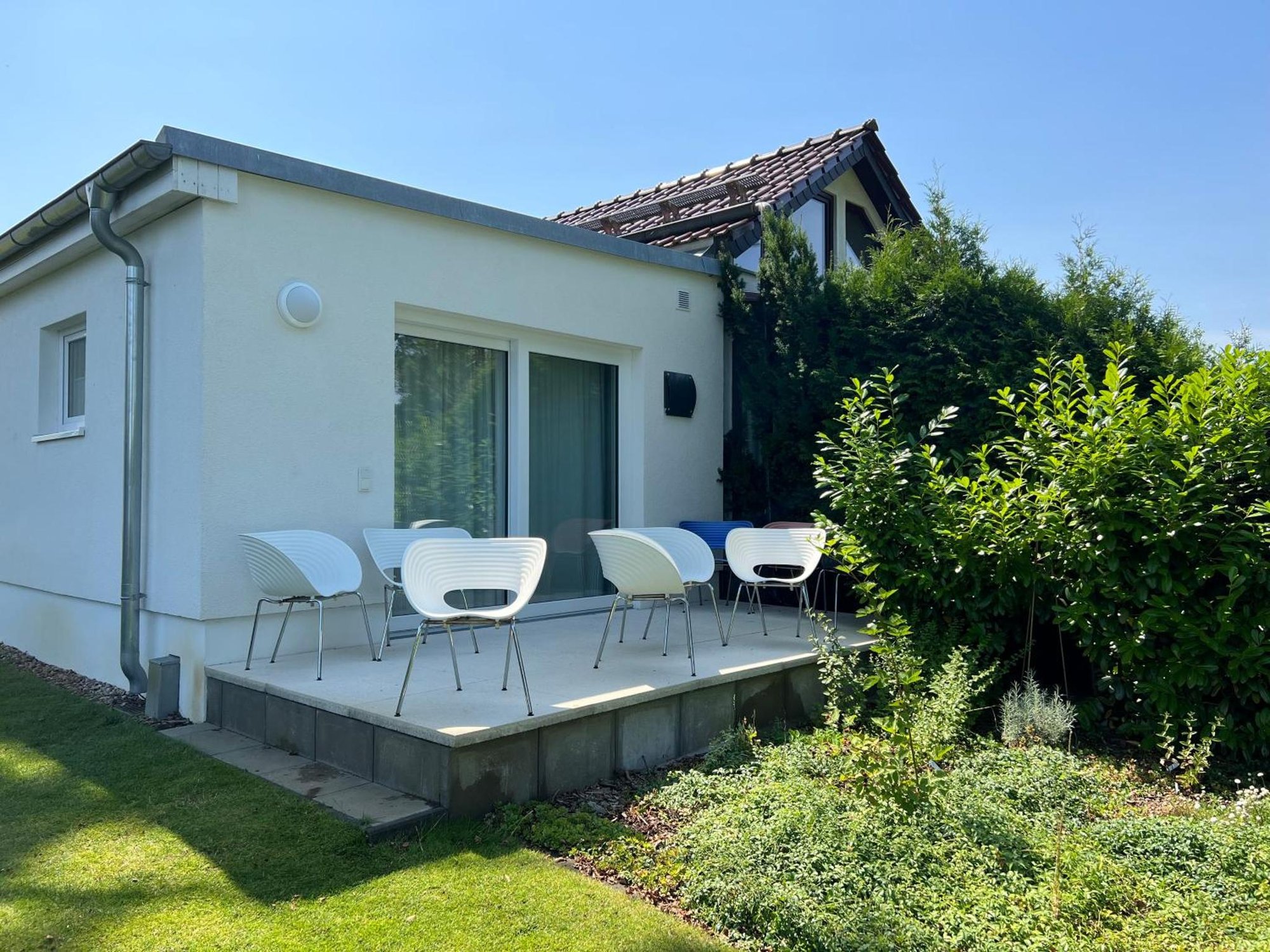 Gästehaus am Großen Zug von außen: weißer Flachdachbau mit Terrasse und weißen Stühlen im Garten