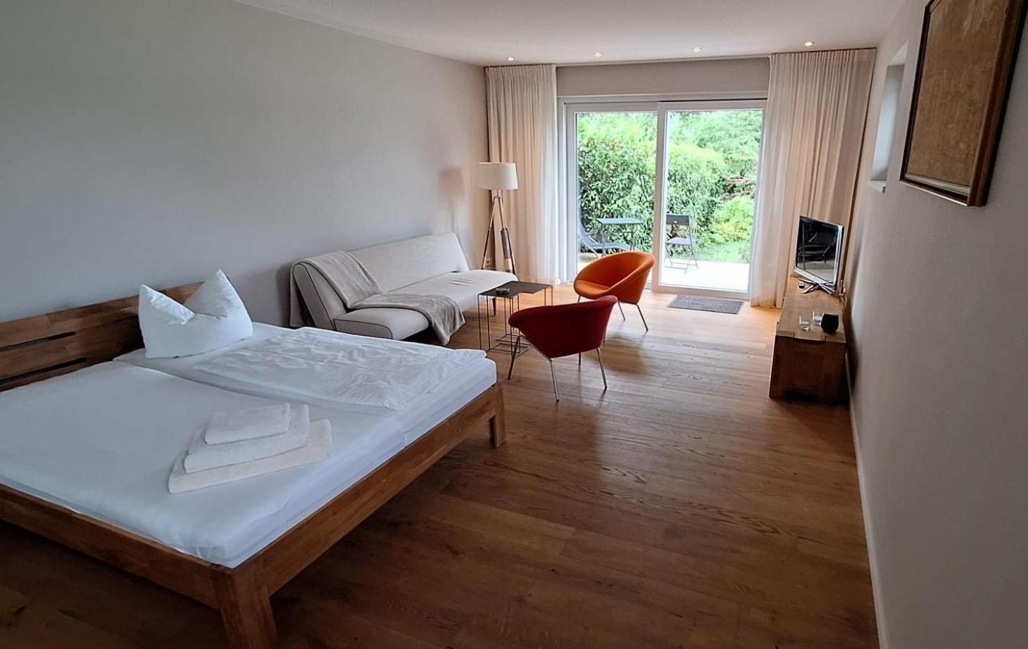 Wohn- und Schlafraum des Gästehauses: Doppelbett, Schlafsofa, Sessel, Parkett, Terrassentür in den Garten