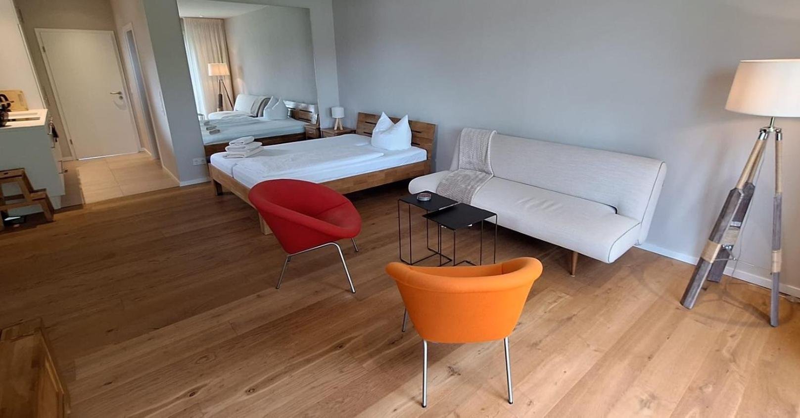 Wohnbereich des Gästehauses mit Schlafsofa, zwei Sesseln und Stehleuchte auf Parkett